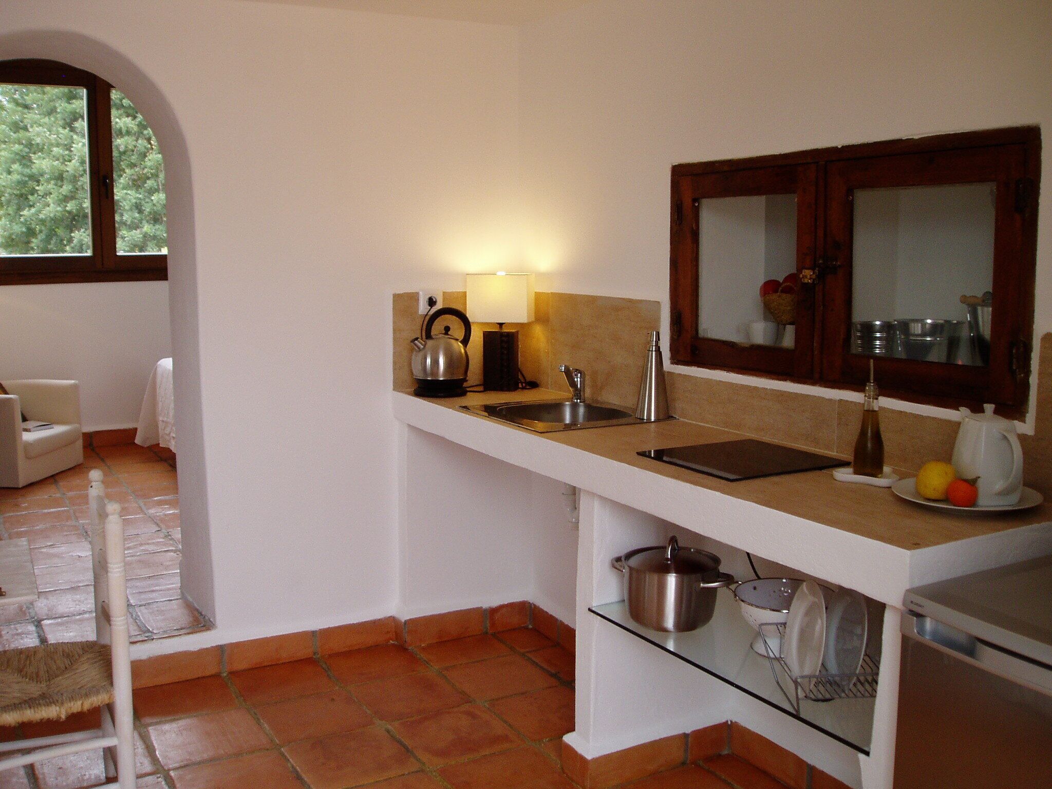 A compact kitchen with a white countertop, a kettle, a sink, and a stove.