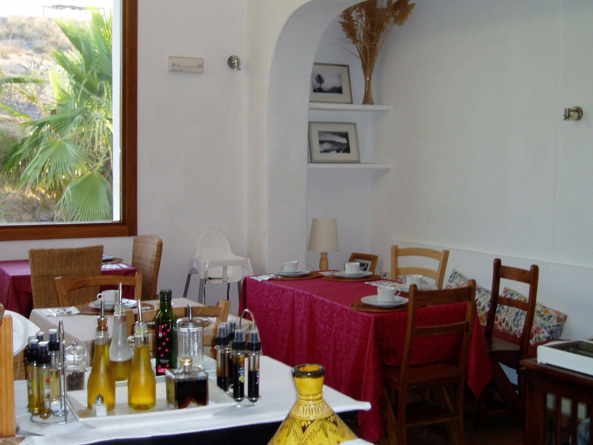 Un comedor con una mesa dispuesta para dos personas, con mantel rojo, platos blancos y diferentes condimentos.