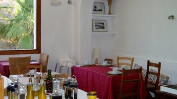 Un comedor con una mesa dispuesta para dos personas, con mantel rojo, platos blancos y diferentes condimentos.