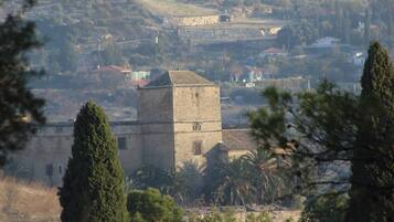A stone tower with a rectangular base and a pointed roof, surrounded by trees and buildings in a hilly landscape.