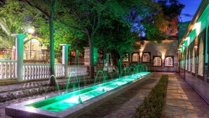 A courtyard with a rectangular water feature, stone flooring, and a building with arched windows and a tiled roof.