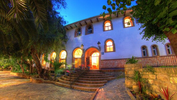 A building with a stone staircase leading to a door, surrounded by greenery and a stone pathway.
