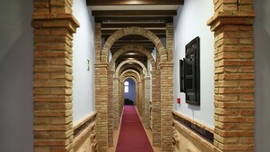 A corridor with brick arches and a red carpet, leading to a distant end.