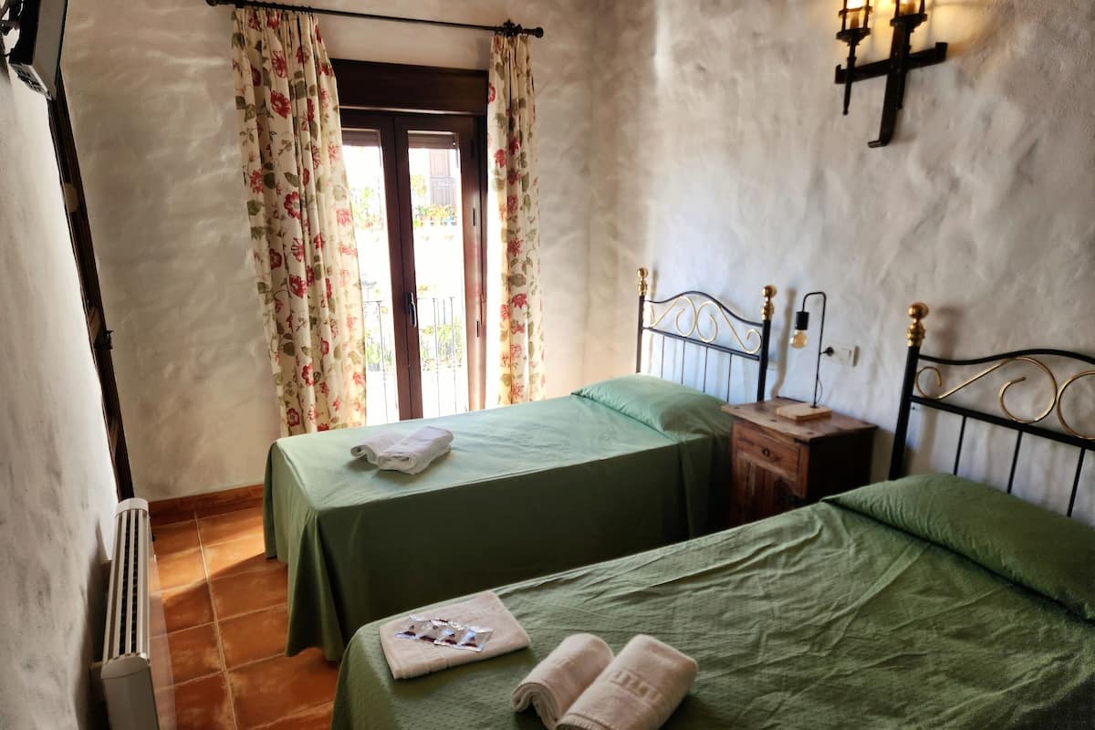 Una habitación con dos camas, un radiador, una mesita de noche y una ventana con cortinas.