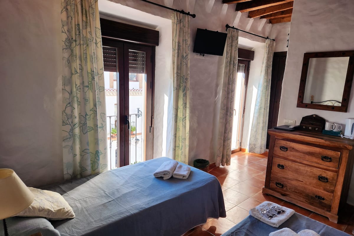 Un dormitorio con cama, cómoda de madera, televisor y balcón con cortinas.