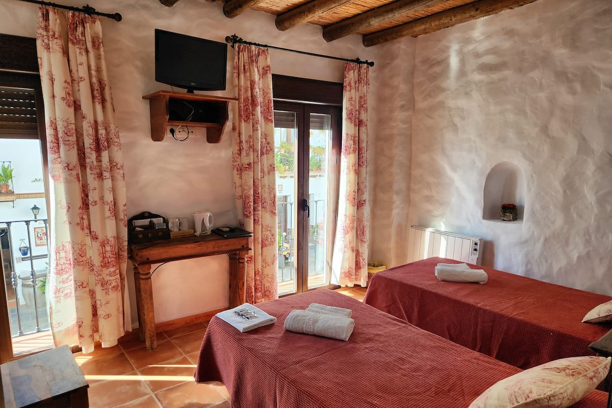 Una habitación con dos camas, televisión, escritorio con hervidor y ventana con cortinas.