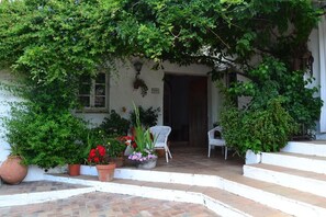 A white building with a covered entrance, potted plants, and a white chair outside.