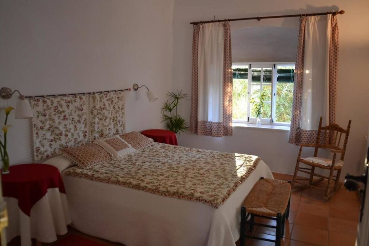 Een slaapkamer met een bed, een stoel, een tafel en een raam met gordijnen.
