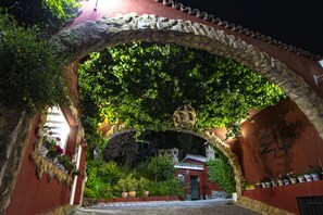 Une entrée en arc surmontée d’une façade en pierre, agrémentée de verdure, et un petit bâtiment doté d’un toit rouge.
