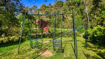 Un parque infantil con columpios y un tobogán en una zona cubierta de césped, rodeado de árboles.