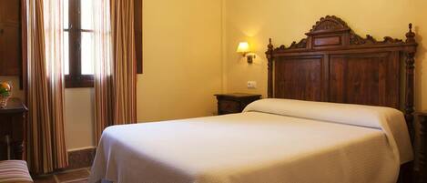 A hotel room with a double bed, a wooden headboard, a nightstand, a lamp, and a window with curtains.