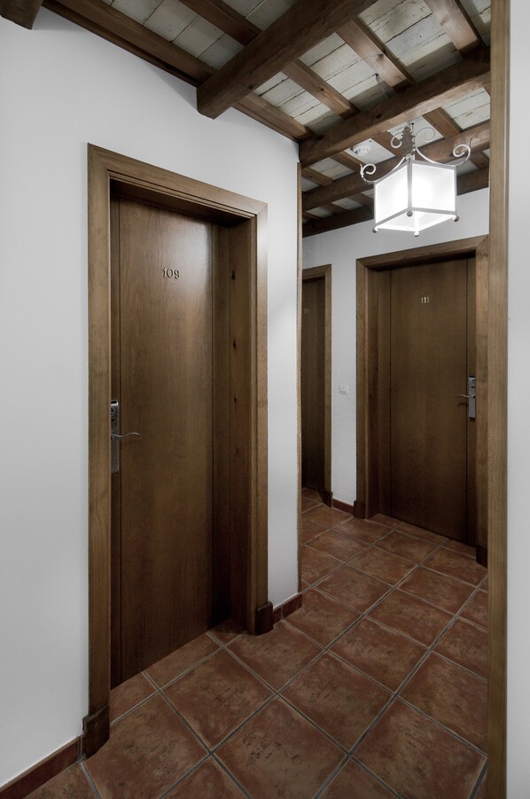 A hallway with wooden doors numbered 109 and 111, a tiled floor, and a hanging light fixture. - Hotel Restaurante Blanco y Verde (Conil de la Frontera)