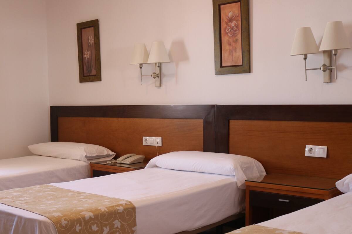 A hotel room with two single beds, a wooden headboard, bedside lamps, a telephone, and a wall-mounted light switch.