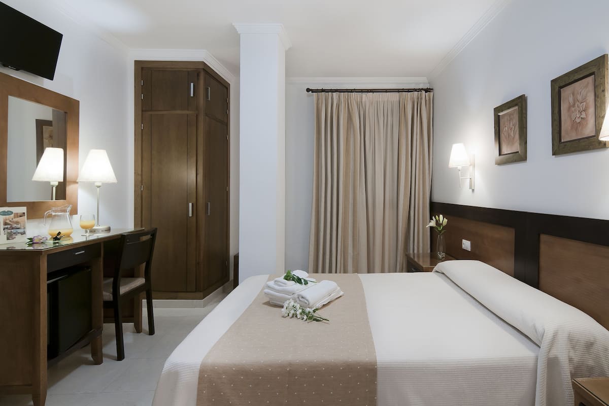 A hotel room with a bed, a desk with a lamp, a wardrobe, and a bathroom with a shower curtain.