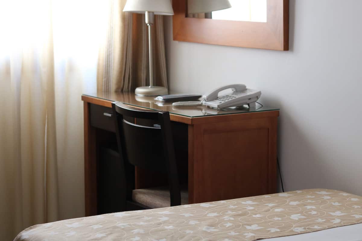 A hotel room with a wooden desk, a telephone, a lamp, and a bed with a patterned bedspread.