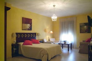 A hotel room with a bed, two chairs, a small table, and a lamp. - Sancho IV Apartamentos Turísticos Rurales (Cortegana)