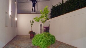 A hallway with a potted plant on a stand, a small statue, and a staircase with greenery. - Sancho IV Apartamentos Turísticos Rurales (Cortegana)