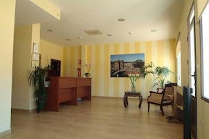 Un área de recepción con un escritorio de madera, un cuadro en la pared y plantas en macetas.