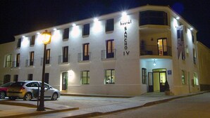 A hotel named 'Sancho IV' with multiple balconies, a well-lit entrance, and a visible car parked in front. - Sancho IV Apartamentos Turísticos Rurales (Cortegana)