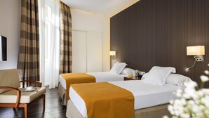 Een hotelkamer met twee bedden, een bureau, een stoel en een raam met gordijnen.