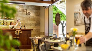 A bar area with a stone wall, wooden furniture, and a counter with a person pouring a drink. - Hotel de Francia y París (Cádiz)