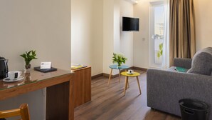 Een moderne woonkamer met een bank, een salontafel, een bijzettafeltje, een aan de muur bevestigde televisie en een raam met gordijnen.