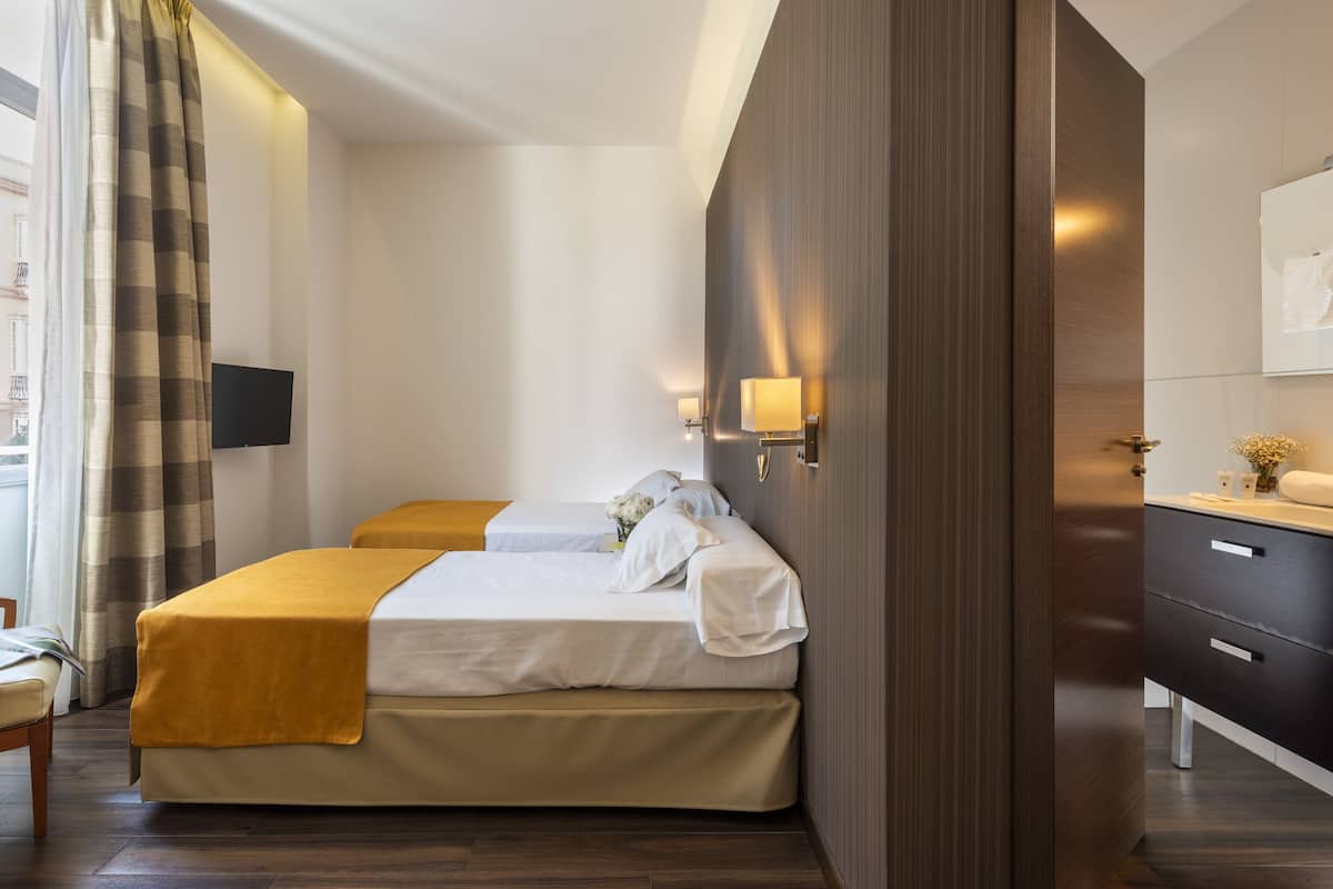 Une chambre d’hôtel avec deux lits, un grand miroir, un téléviseur à écran plat et une armoire en bois.