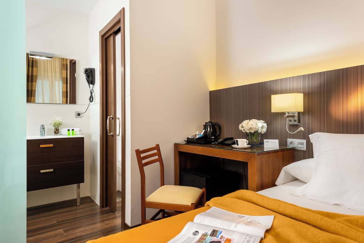Une chambre d’hôtel comprenant un lit, un bureau avec une lampe, une chaise, une coiffeuse avec un miroir et un sèche-cheveux.