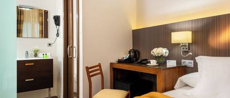 Habitación de hotel con cama, escritorio con lámpara, silla, tocador con espejo y secador de pelo.