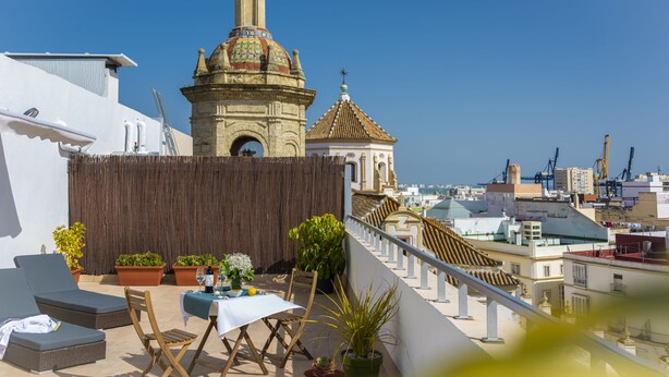 Een terras op het dak met een eettafel, plantenbakken en uitzicht op een historische toren.