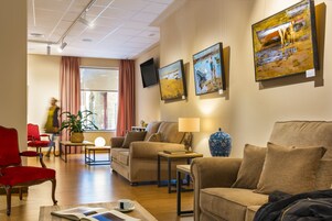 A hotel lobby with a red armchair, beige sofas, a coffee table, and artwork on the walls.