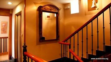 Una escalera con barandas de madera y un pasamanos rojo, que conduce a una habitación con un espejo grande y una lámpara de pared.