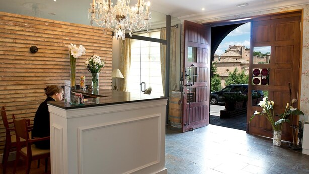 Zona de recepción con pared de madera, candelabro y una puerta grande de madera que da al exterior.
