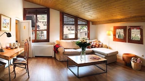 Un salón acogedor con techo de madera, un sofá, una mesa de centro y vistas amplias a través de grandes ventanales.