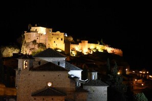 Un château historique aux murs et aux tours illuminés, entouré d’un rempart et de bâtiments plus modestes.