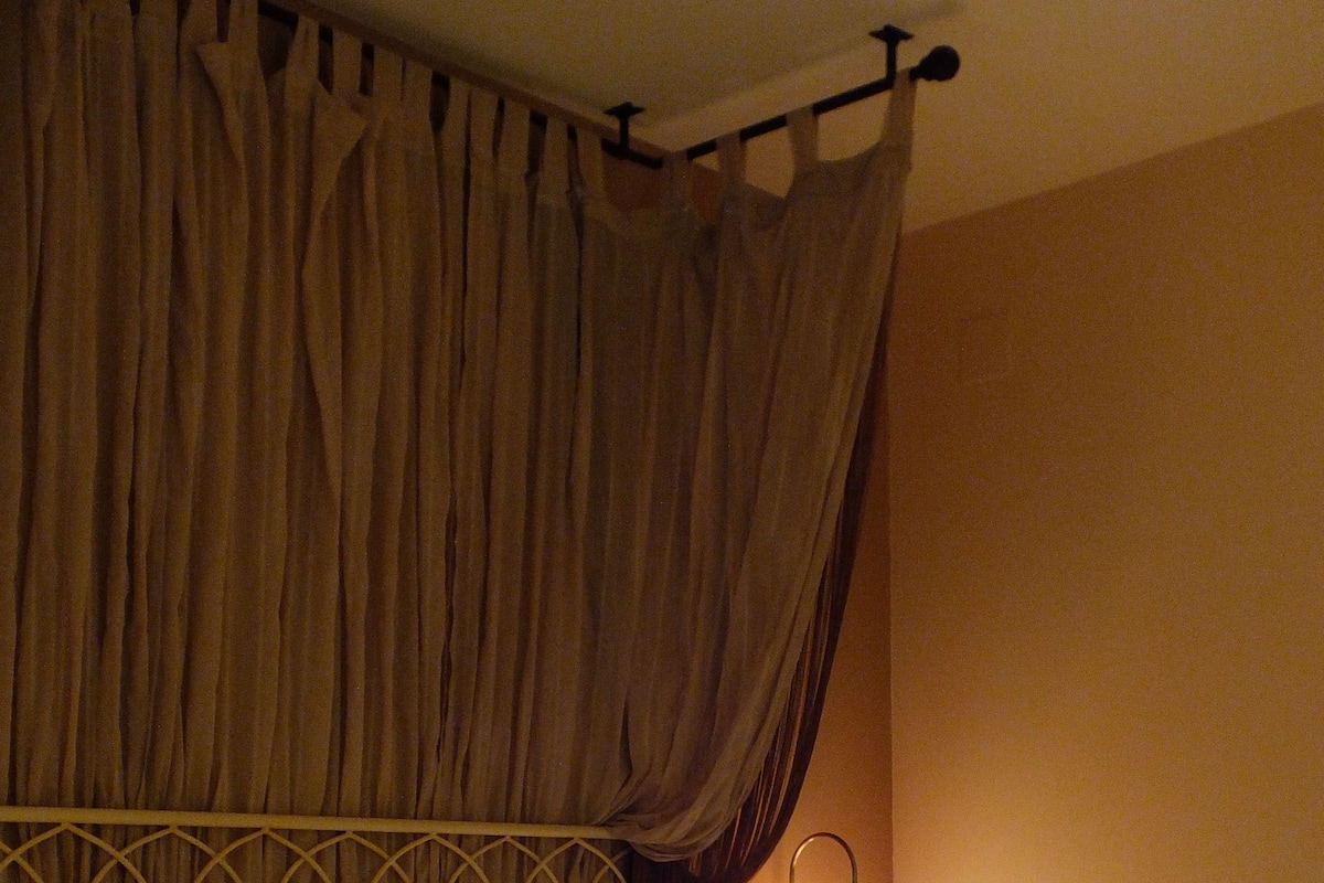 A bed with a metal headboard, a bedside table with a lamp, and a curtain.