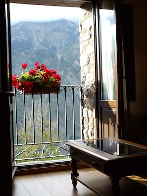 Un balcón con una jardinera de flores, un banco de madera y vistas a montañas.