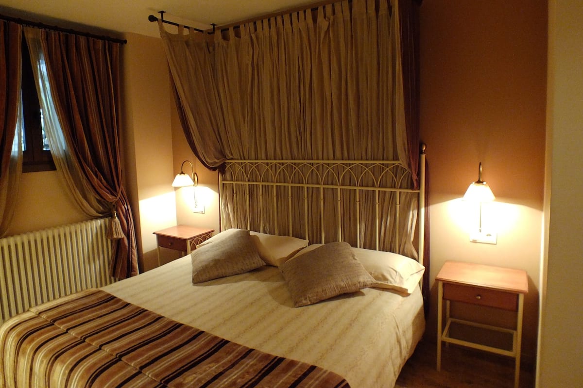 A bedroom with a bed, two bedside tables, a radiator, and curtains.