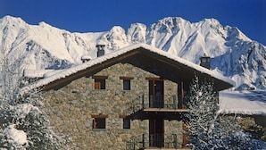 A stone chalet with a balcony, set against a backdrop of snow-covered mountains. - Hotel Casa Cornel (Benasque)