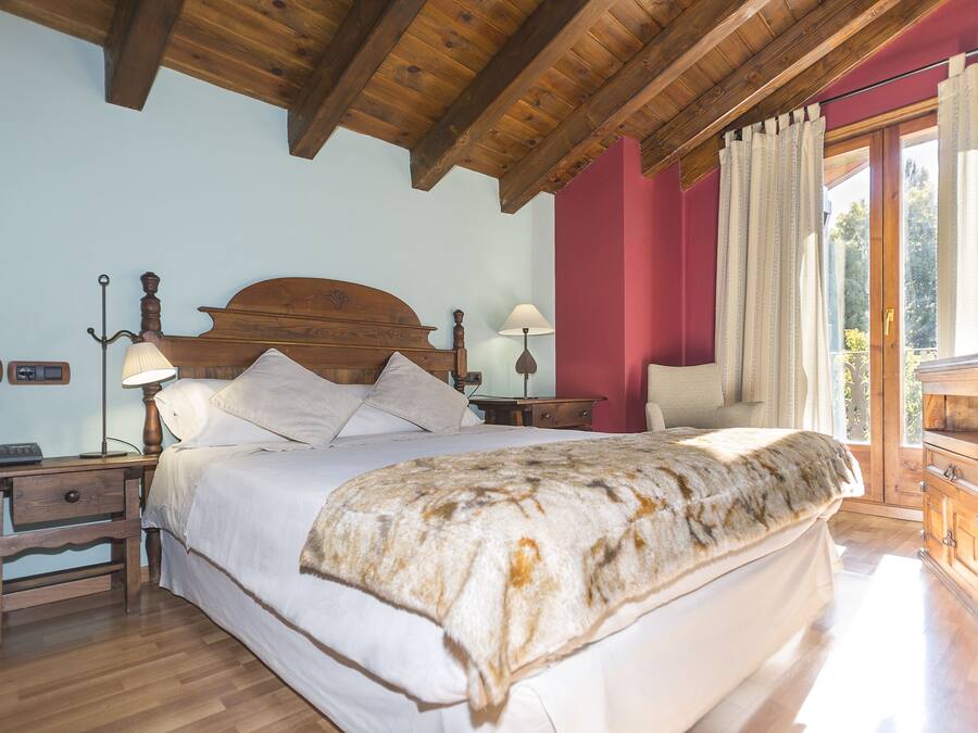 A bedroom with a wooden ceiling, a bed with a white bedspread, a nightstand with a lamp, and a wooden dresser.