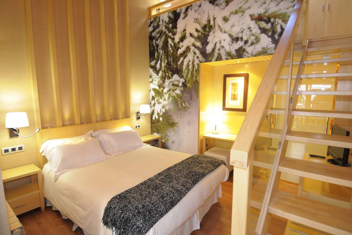 A hotel room with a bed, nightstands, a lamp, a painting, and a wooden staircase.