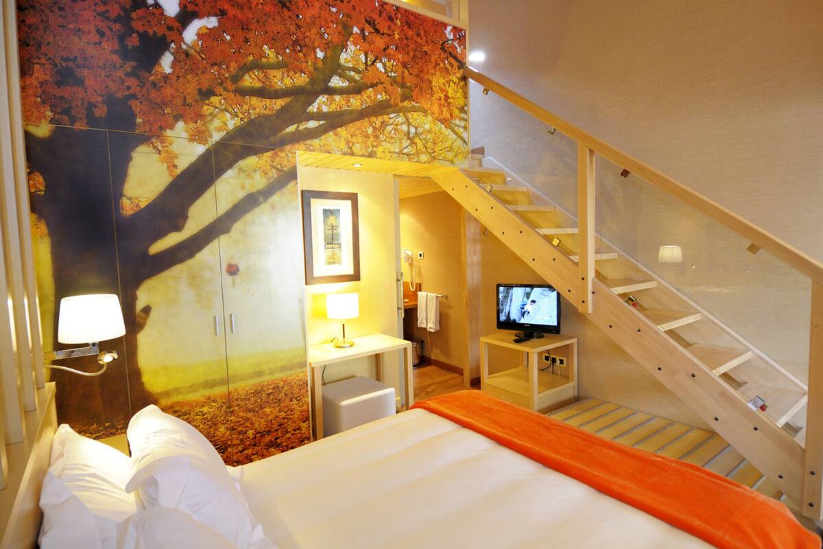 A hotel room with a bed, a desk with a lamp, a television, and a staircase.