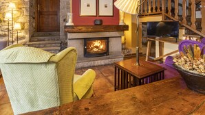 A cozy living room with a stone fireplace, a wooden staircase, and a television. - Hotel Casa Cornel (Benasque)