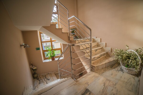 A marble staircase with metal railings, a potted plant, and a window with a view.