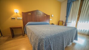 Ein Hotelzimmer mit einem hölzernen Kopfteil, einem Nachttisch, einem Beistelltisch und einem großen Bett mit blauer Bettdecke.