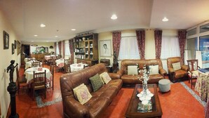 A spacious living room with leather sofas, a coffee table, and a dining area with a table set for four. - Hotel La Rivera (Cabrales)
