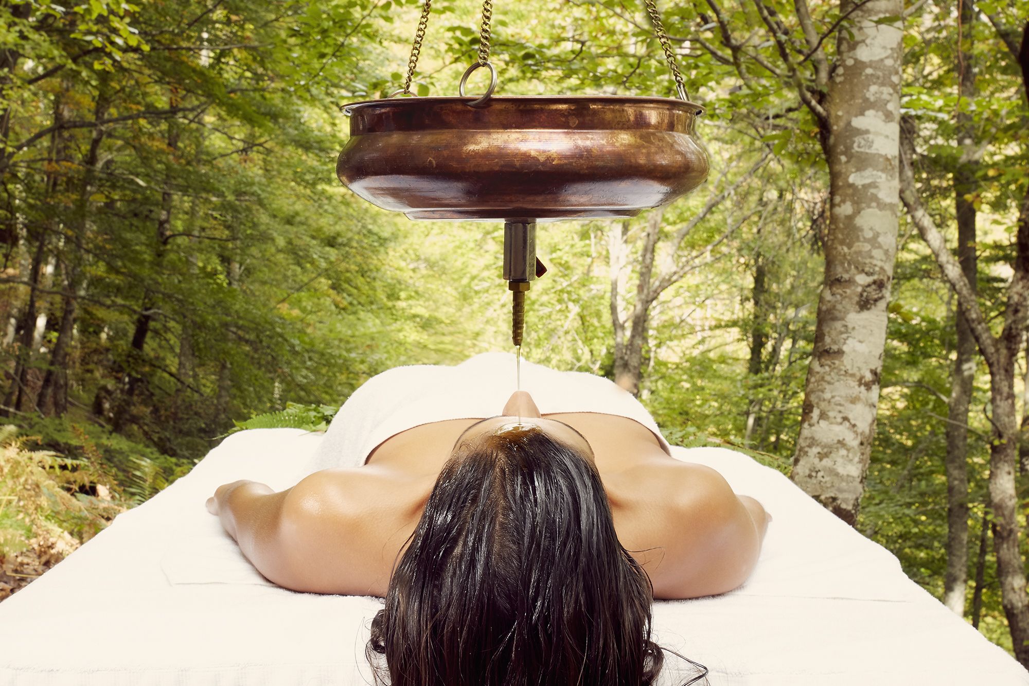 A person lying face down on a massage table in a forest setting.