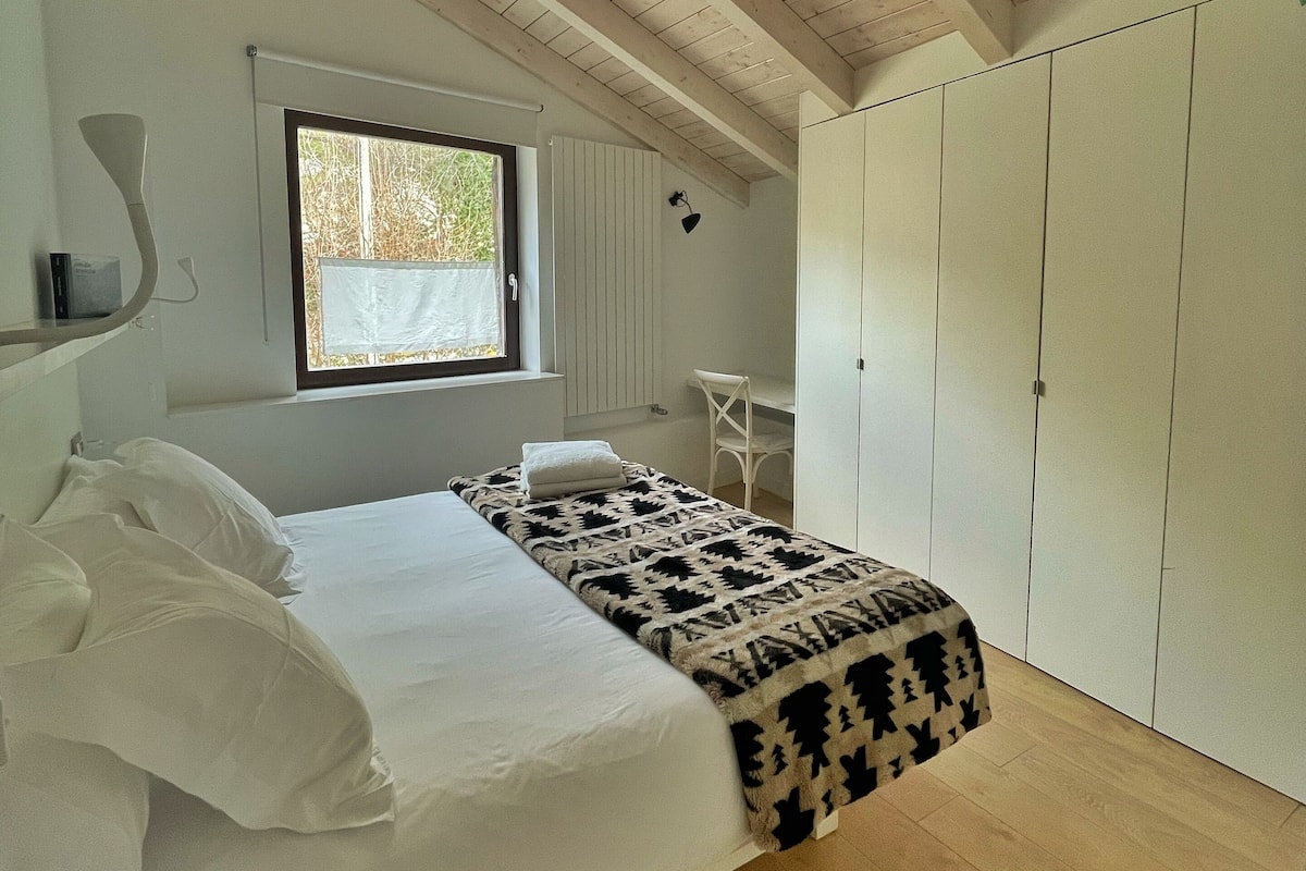 A bedroom with a bed, a window, a wardrobe, and a desk.