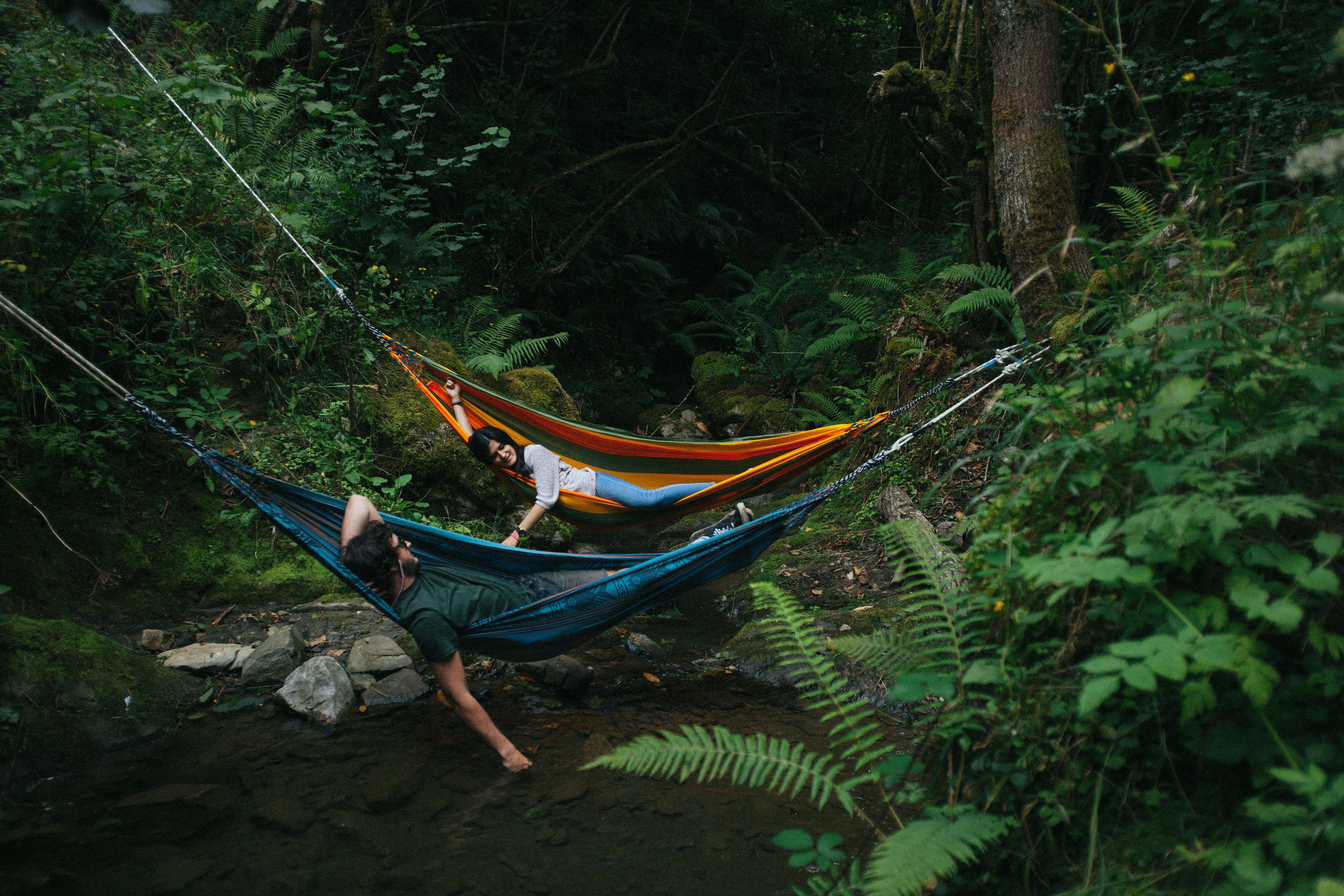 A hammock in a forested area with a person lying in it.