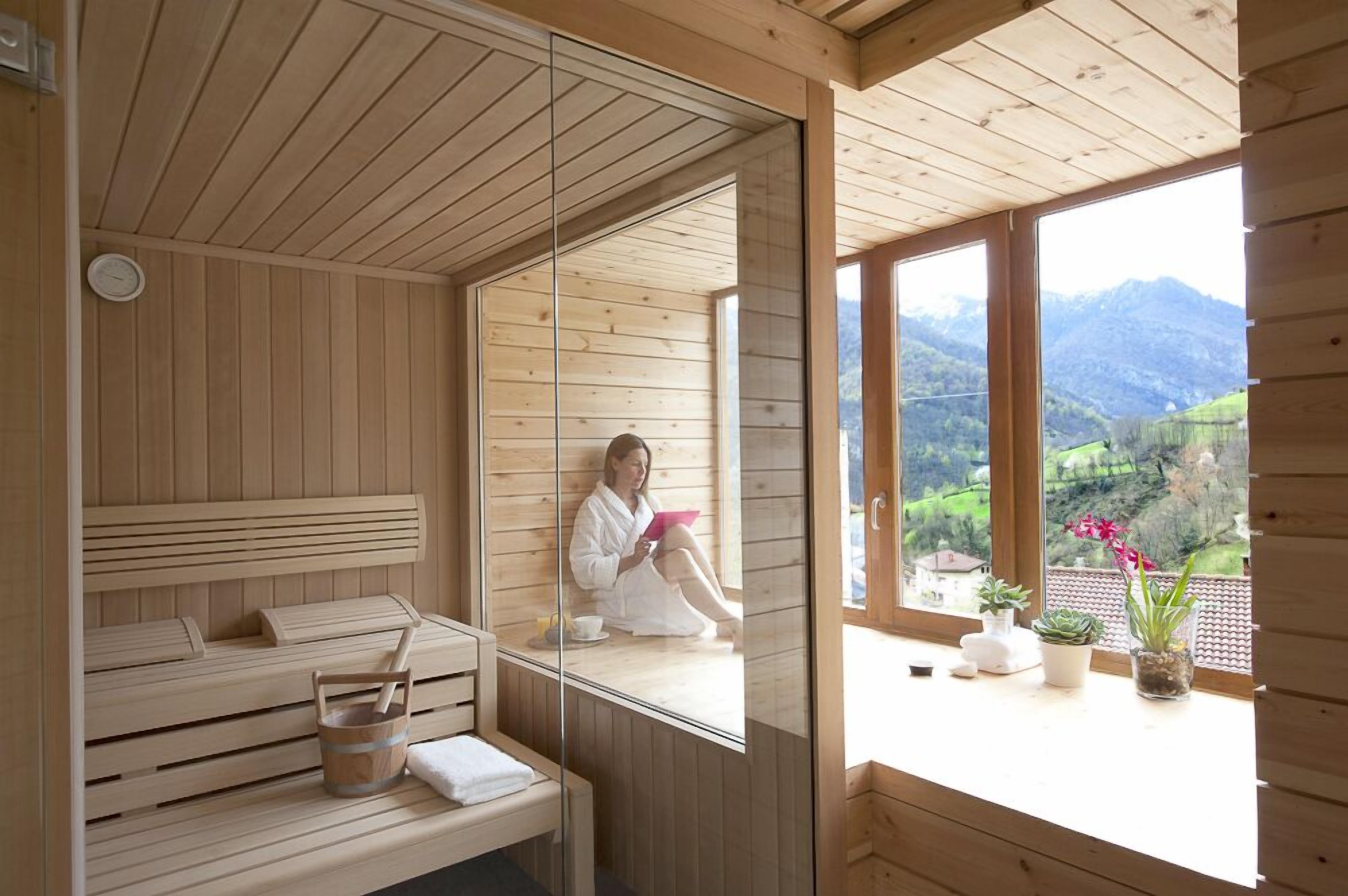Una sauna de madera con un banco, un balde y una ventana que ofrece vistas a un paisaje verde.